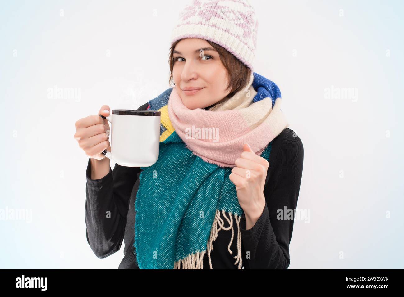Ritratto di una donna sorridente in un cappello e una sciarpa invernali con una tazza in mano. Concetto di malattie virali. Supporti misti Foto Stock
