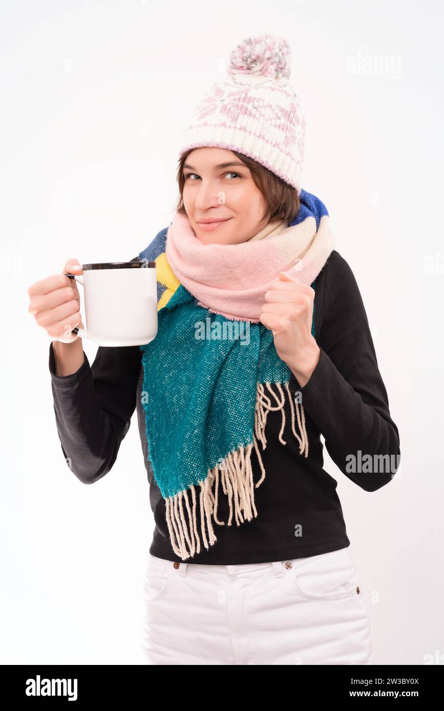 Ritratto di una donna sorridente in un cappello e una sciarpa invernali con una tazza in mano. Concetto di malattie virali. Supporti misti Foto Stock