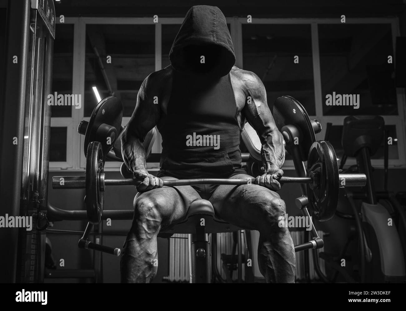 Immagine in bianco e nero di un potente atleta con una felpa con cappuccio seduta su una panchina in palestra. Concetto di fitness e bodybuilding Foto Stock