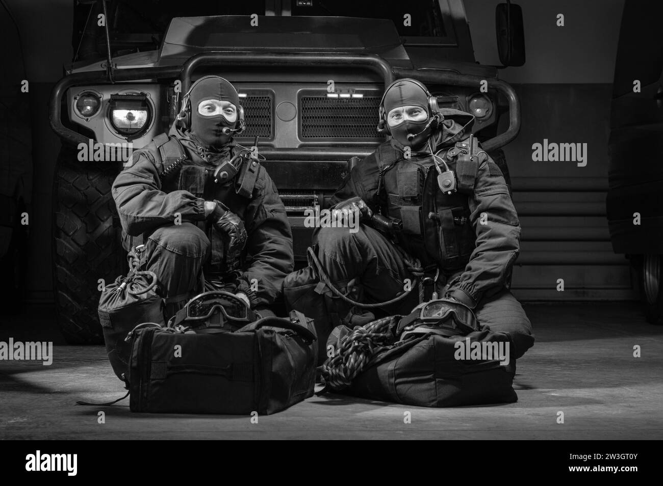 Due commando in uniforme siedono in un hangar con un camion militare sullo sfondo. Concetto SWAT. Supporti misti Foto Stock