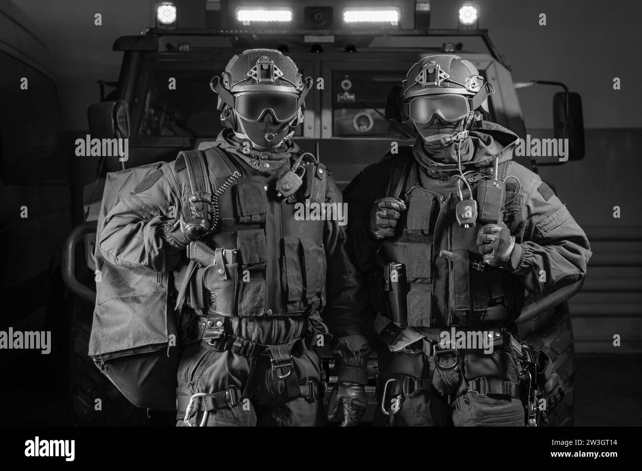 Due uomini in uniforme militare stanno in un hangar con un camion sullo sfondo. Concetto SWAT. Supporti misti Foto Stock