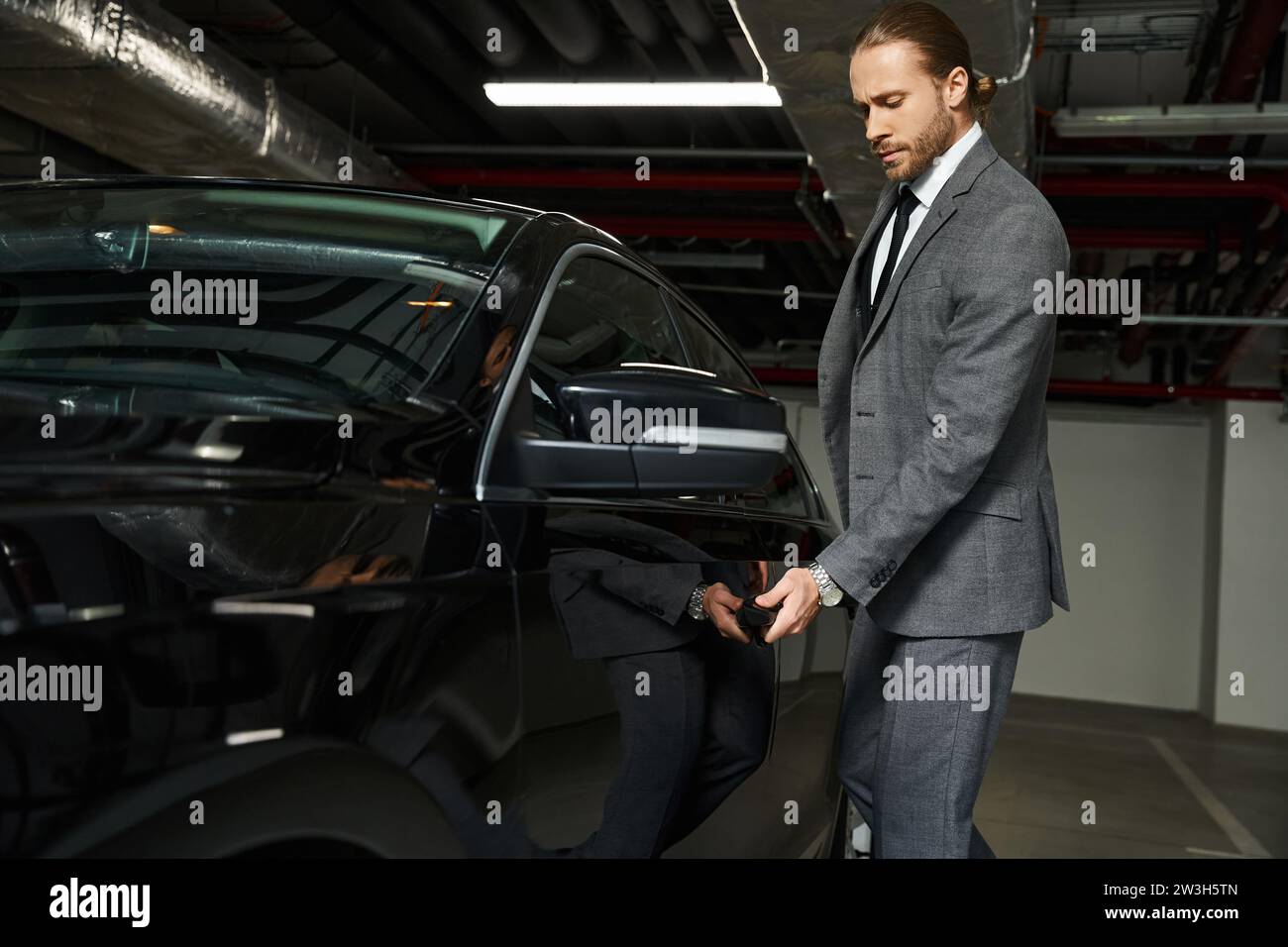 elegante e attraente uomo d'affari in tuta elegante con porta a cravatta della sua auto nel parcheggio Foto Stock