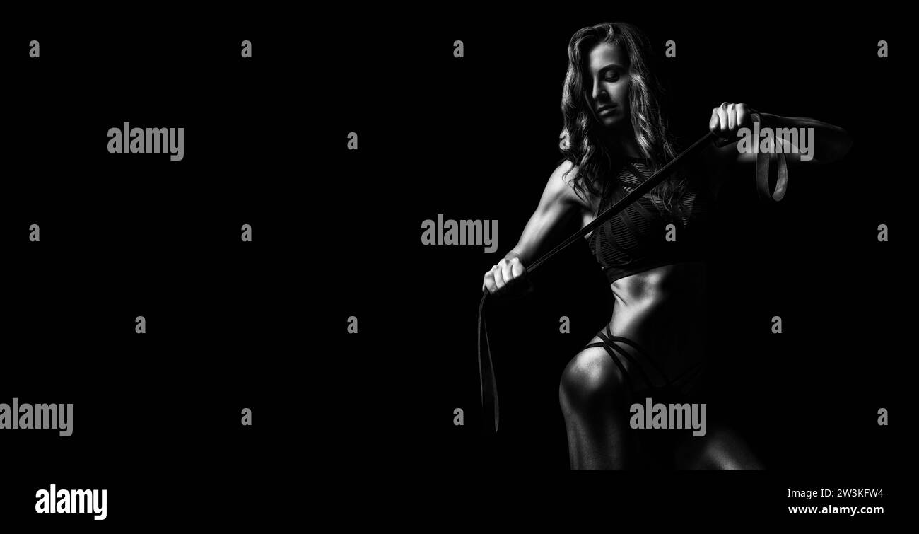 Bellissima ragazza in posa con una fascia elastica da ginnastica su sfondo nero. Sport, fitness e bodybuilding. Supporti misti Foto Stock