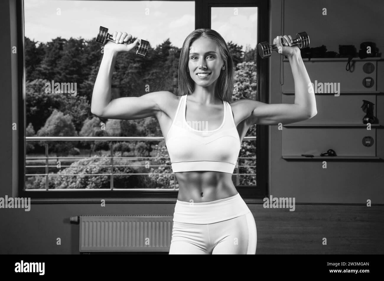 L'affascinante giovane atleta si sta allenando con i manubri in palestra. Concetto di bodybuilding. Sport. Sollevamento pesi. Supporti misti Foto Stock