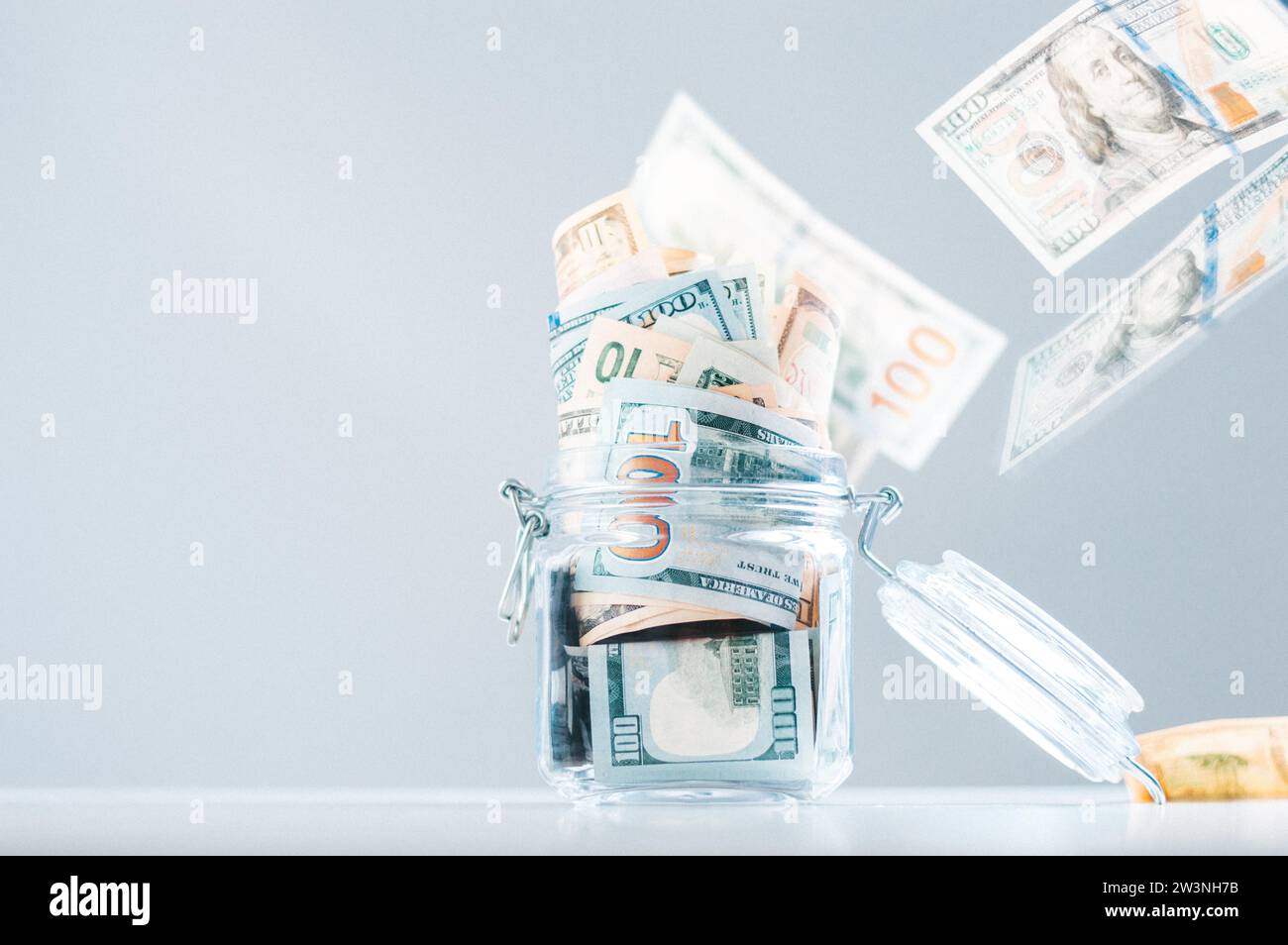 Salvadanaio di vetro pieno di soldi. Le banconote sono strisciate dall'alto. Il concetto di sperperamento. Supporti misti Foto Stock