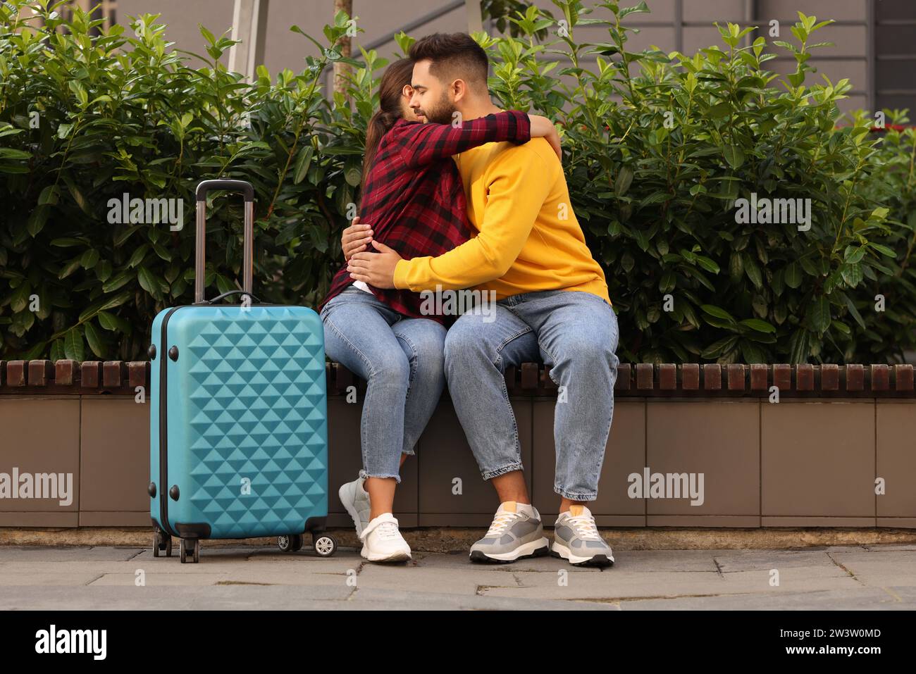 Relazione a distanza. Bella coppia che abbraccia la panca e la valigia all'aperto Foto Stock