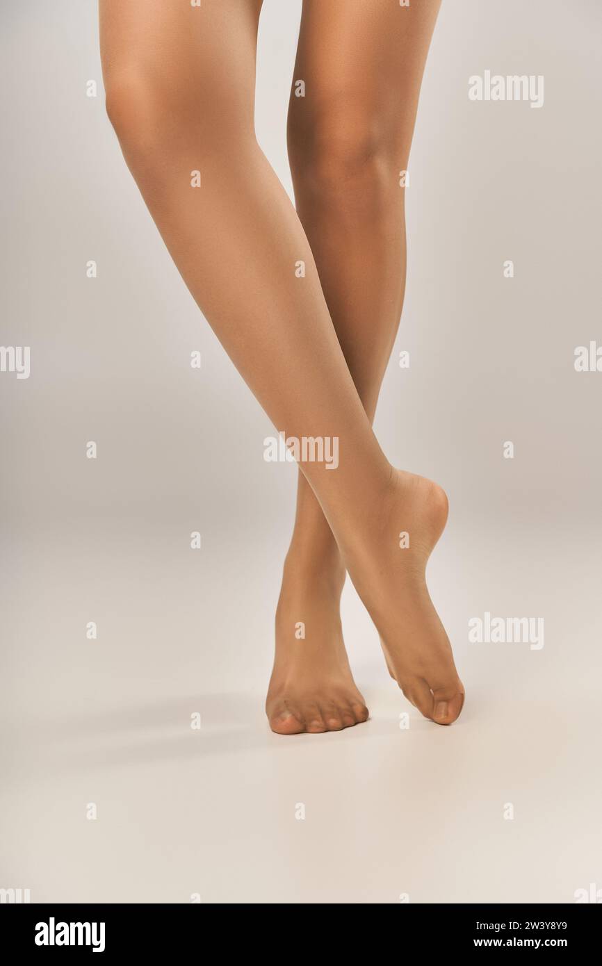 vista parziale della giovane donna in collant beige senza cuciture che posa su sfondo grigio, calze Foto Stock