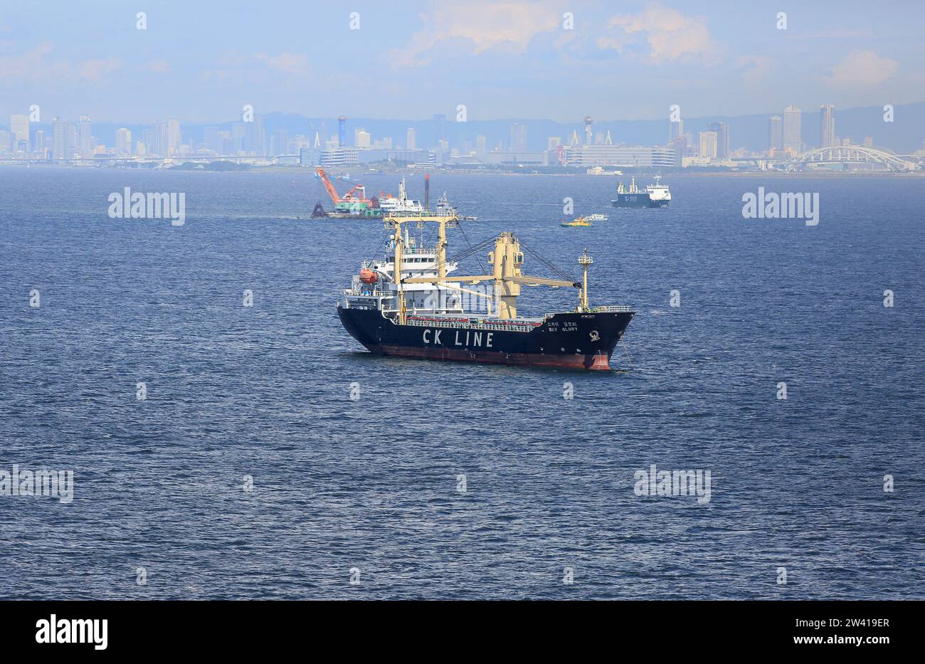 La nave da carico generale sudcoreana Sky Glory, compagnia di navigazione coreana CK Line, nella zona della baia di Osaka, Giappone, il ponte Yumemai e lo skyline della città di Osaka sullo sfondo Foto Stock