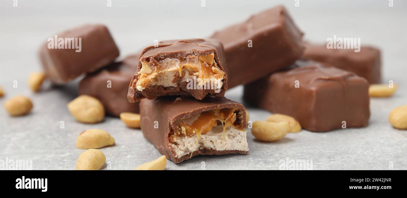 Barrette di caramelle al cioccolato con caramello, noci e torrone sul tavolo grigio chiaro, primo piano. Design banner Foto Stock