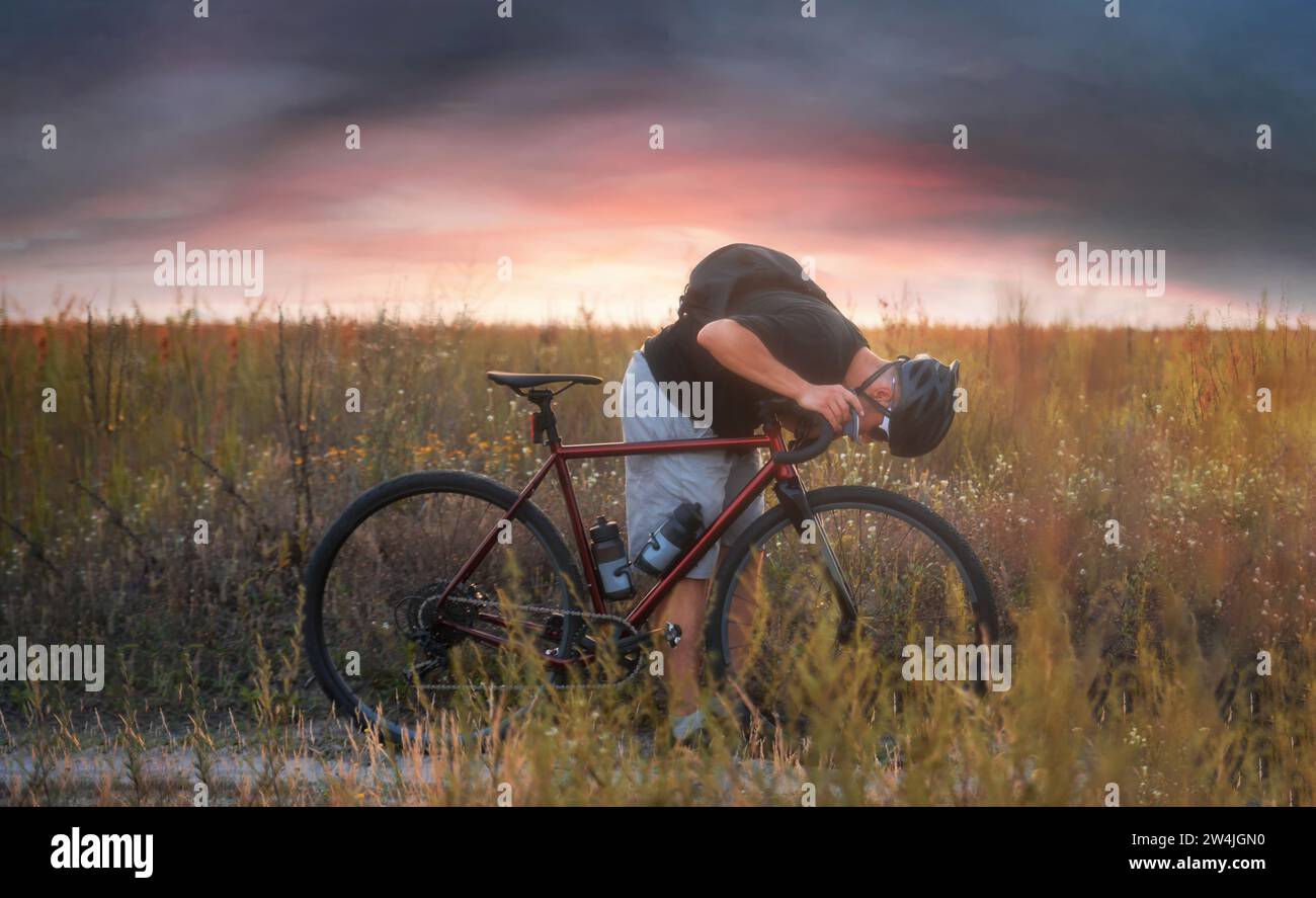 Ciclista sul campo che controlla la sua ruota anteriore. Avventure in bicicletta. Foto Stock