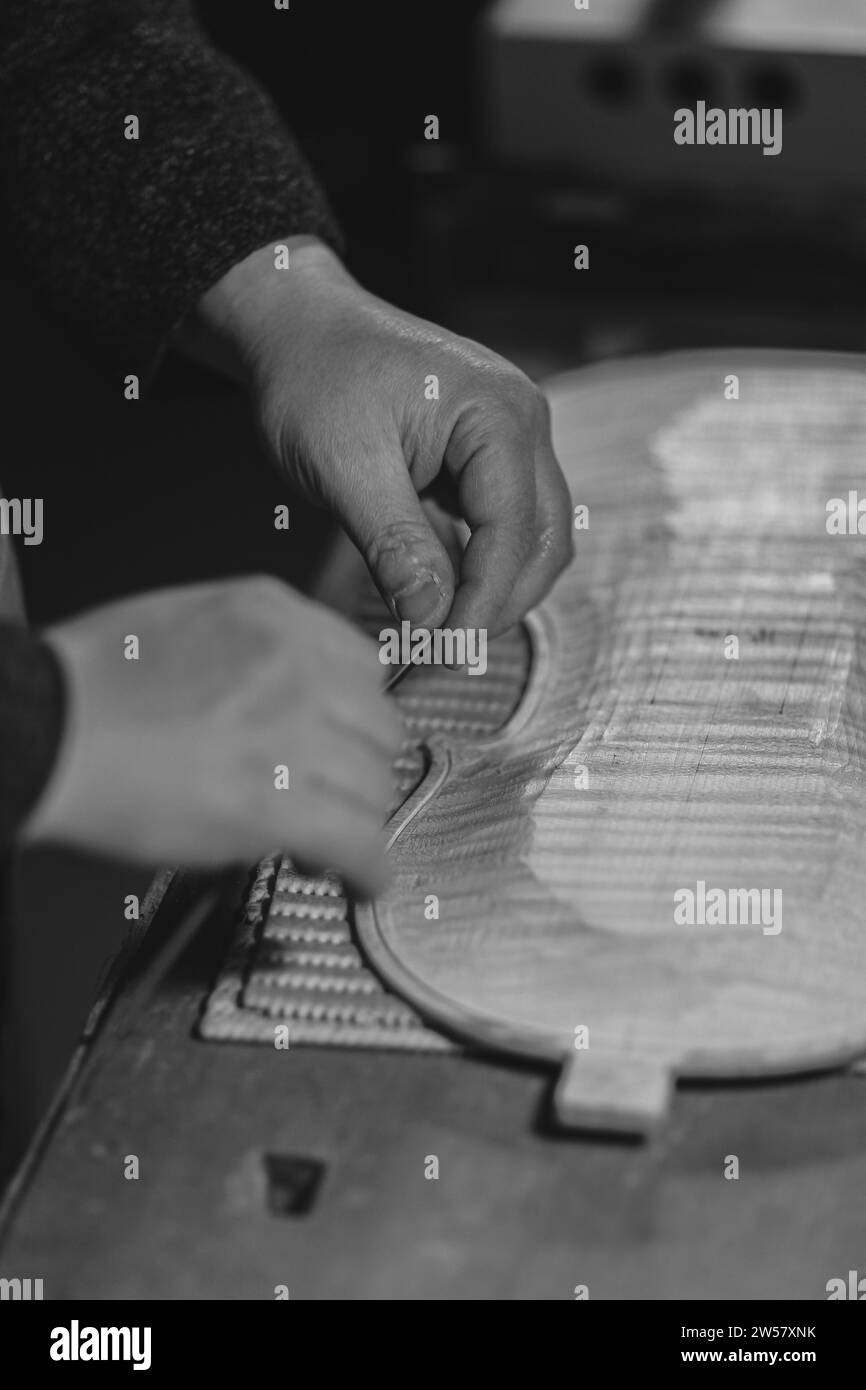 Un artigiano liutaio irriconoscibile lavora con le mani nella sua officina prova a spingere e incollare strisce di filetto in un canale di legno intagliato, per una novità Foto Stock