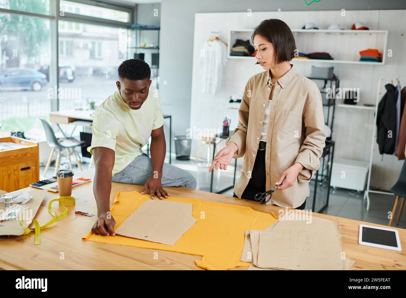 giovani designer di abiti multiculturali che lavorano con modelli di cucito in uno studio di stampa professionale Foto Stock