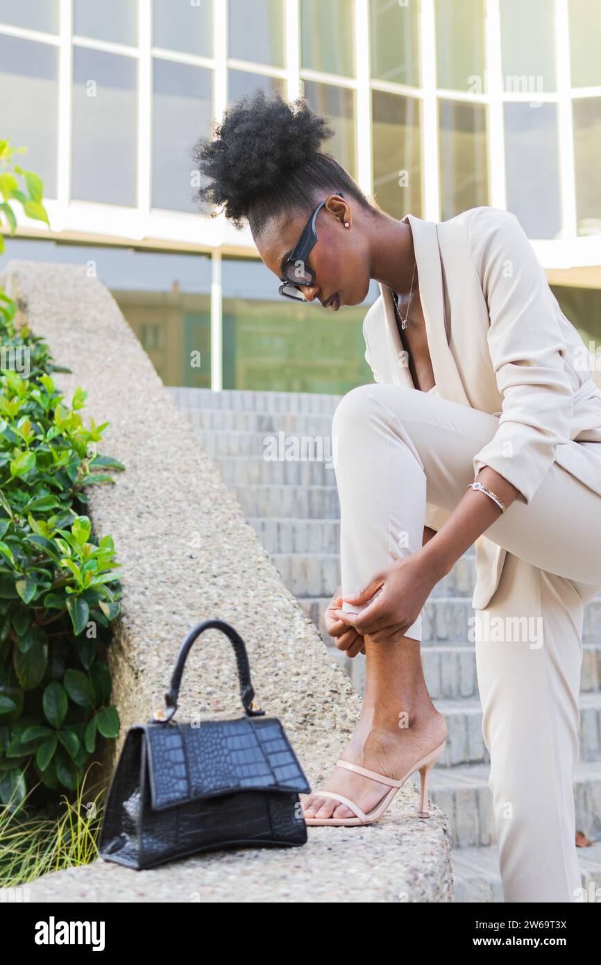 Vista laterale di una giovane imprenditrice afroamericana alla moda, con pantaloni regolabili mentre si calpestano sul muro di contenimento Foto Stock