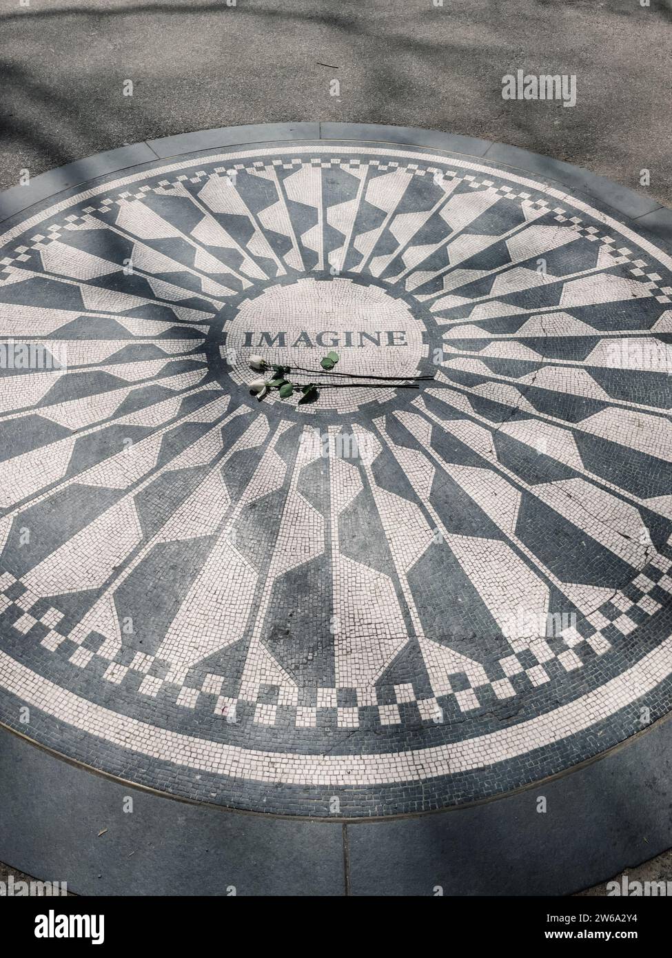 Alto angolo di Imagine memoriale con iscrizione circolare e mosaico a motivi con rose bianche su gambo verde alla luce del giorno a Manhattan New York Foto Stock