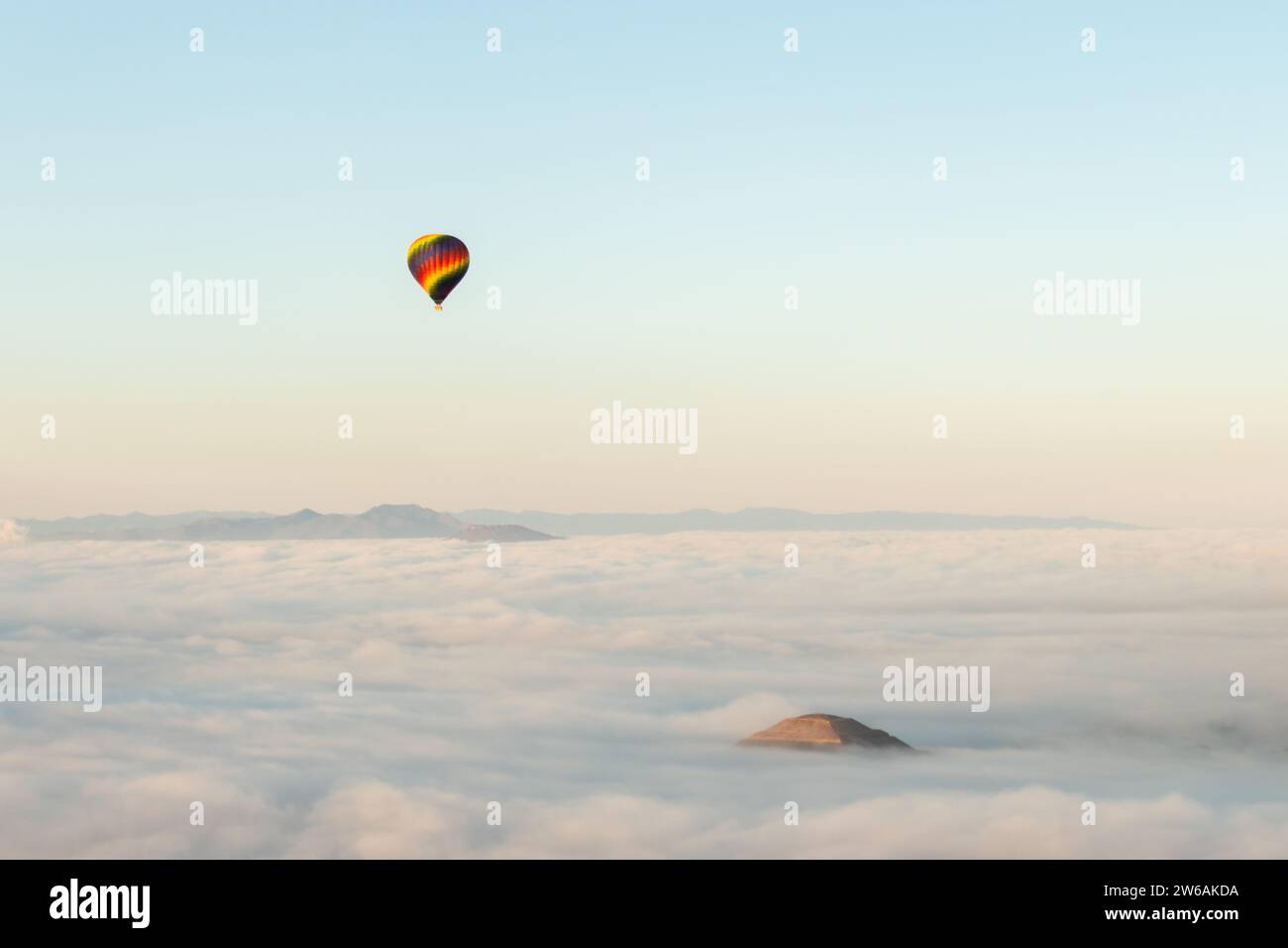 Una mongolfiera solitaria galleggia su un mare di nuvole all'alba, con un picco solitario della Piramide del Sole che emerge dal paesaggio nebbioso di Foto Stock