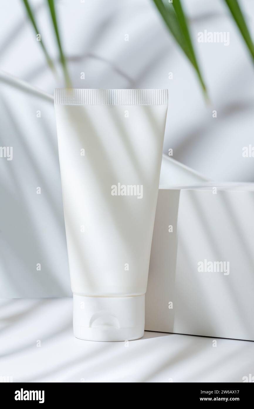 Un tubo cosmetico bianco bianco si trova su un piedistallo con un'ombra di foglie di palma che si getta su di esso, suggerendo una cura naturale della pelle Foto Stock