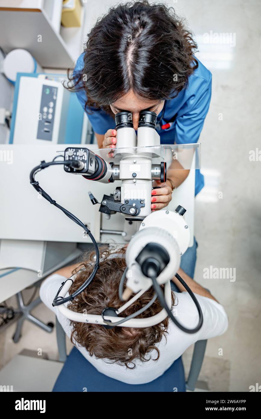 Vista dall'alto di medico femminile anonimo in uniforme medica e con stetoscopio guardando lontano mentre seduto con paziente maschile anonimo a split lamp biomi Foto Stock