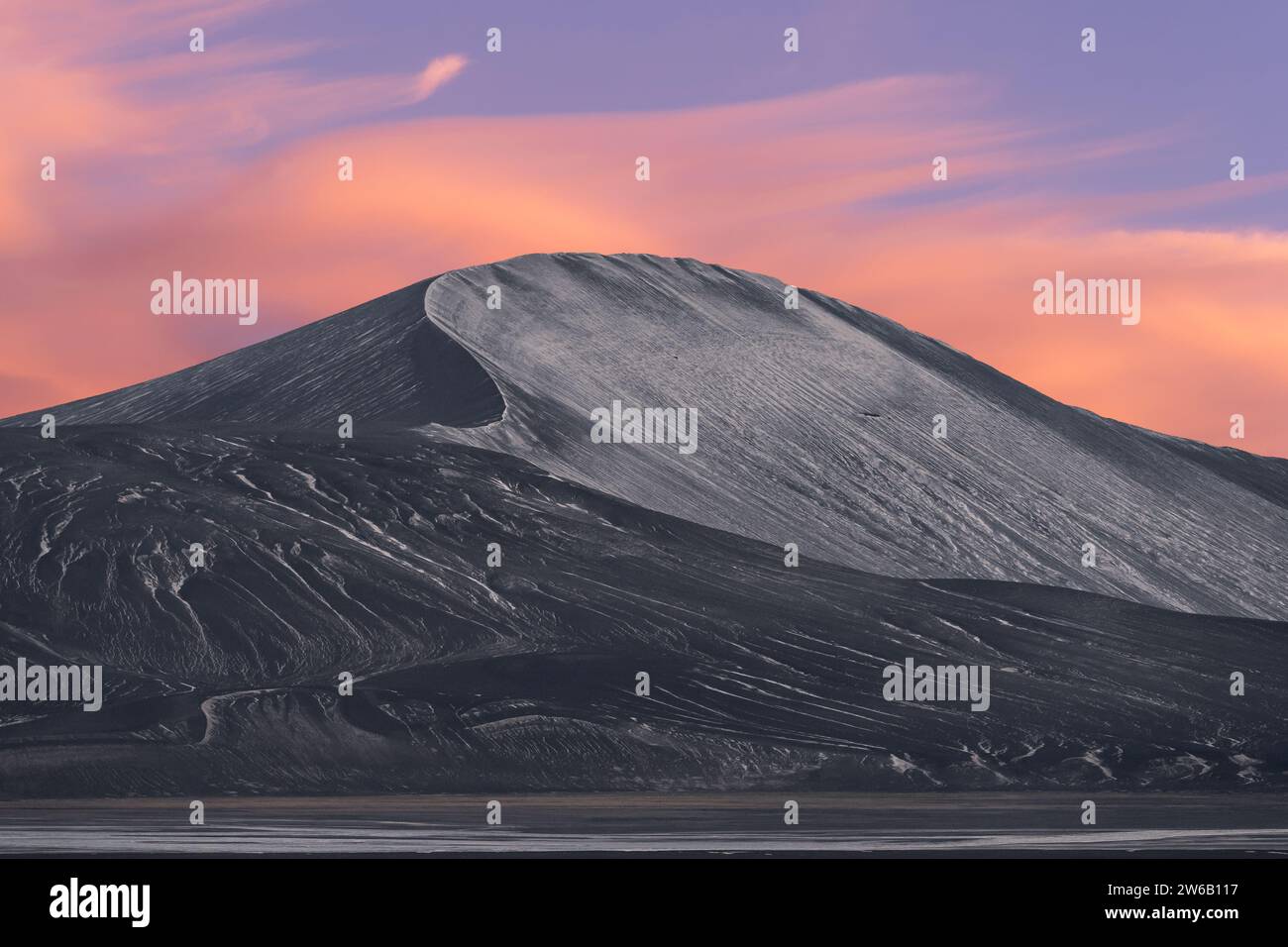 Una scena tranquilla in Islanda caratterizzata da una montagna graziosamente in pendenza spolverata di neve sullo sfondo di soffici cieli rosa crepuscolo. Foto Stock