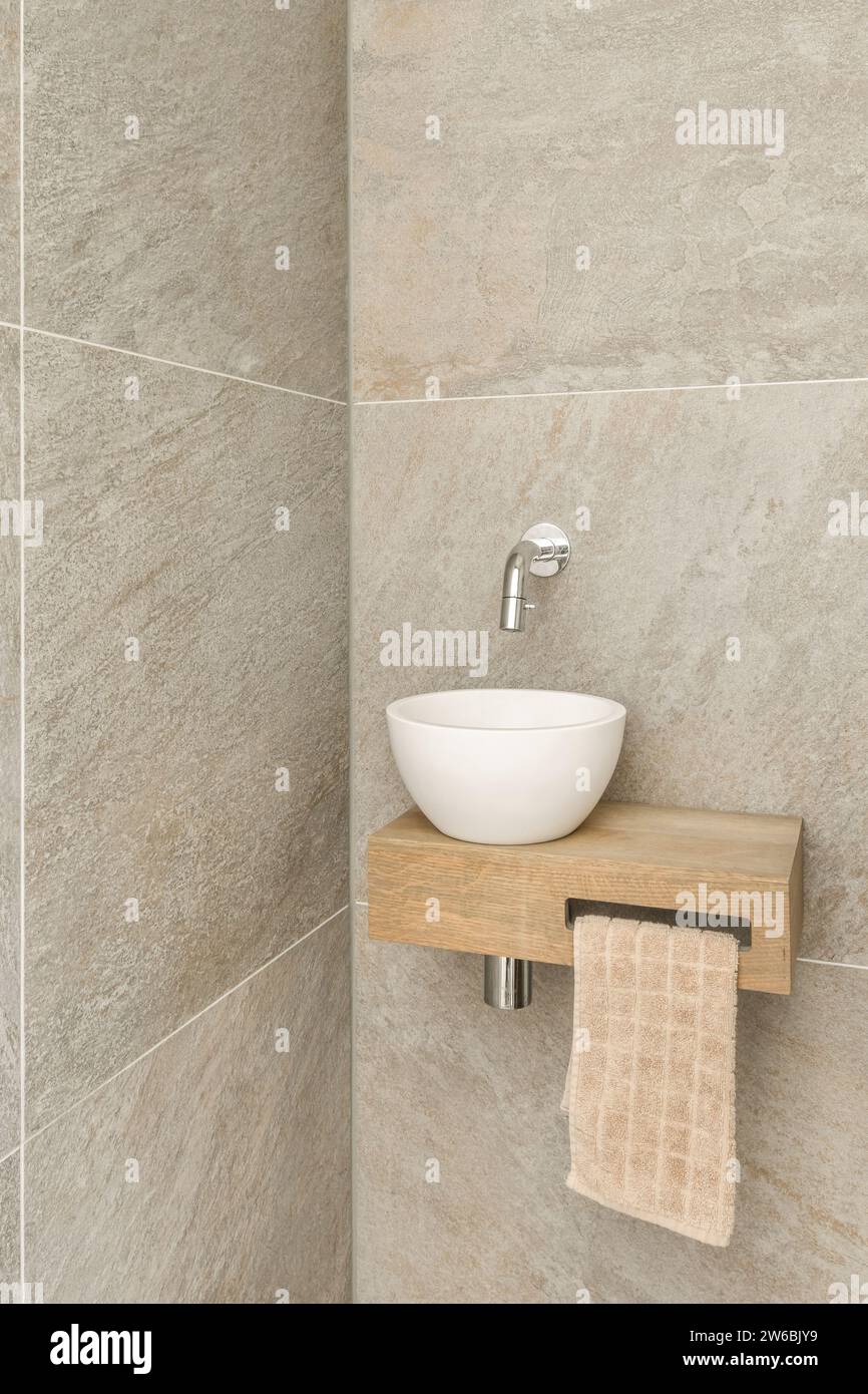 Rubinetto montato a parete su lavabo in ceramica bianca su ripiano in legno con asciugamano appeso in bagno Foto Stock