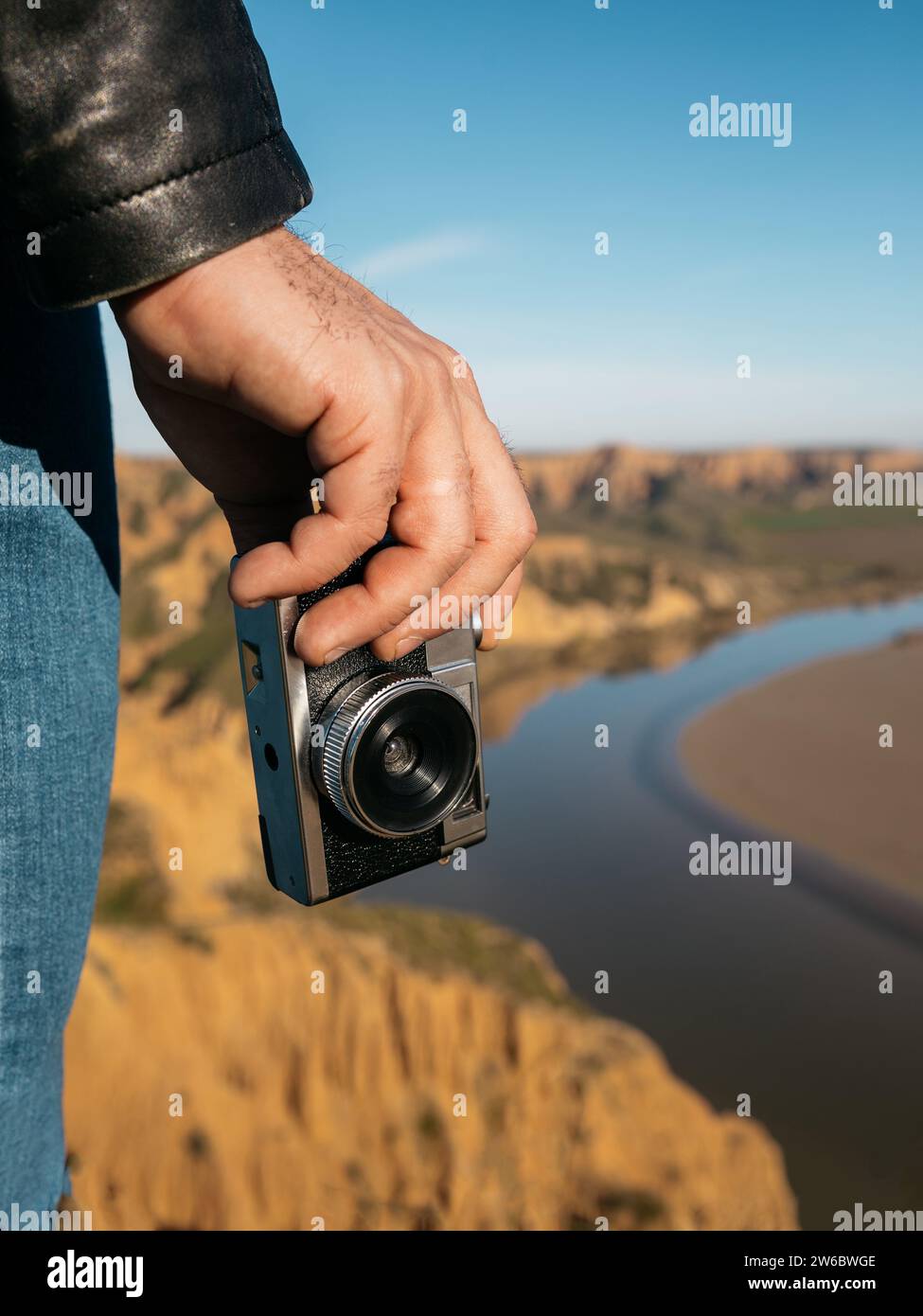 Primo piano della mano di un viaggiatore che tiene in mano una macchina fotografica vecchio stile con uno scenografico paesaggio fluviale sullo sfondo Foto Stock