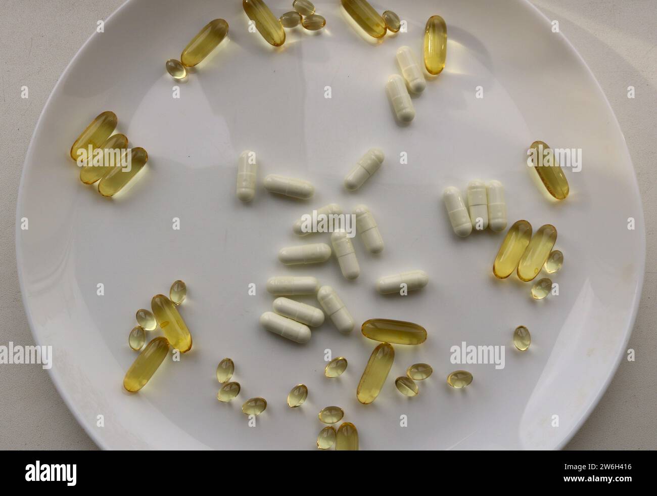 un grande piatto bianco con una dispersione di capsule bianche e dorate con vitamine, un integratore alimentare biologico sotto forma di complesso di vitamine Foto Stock