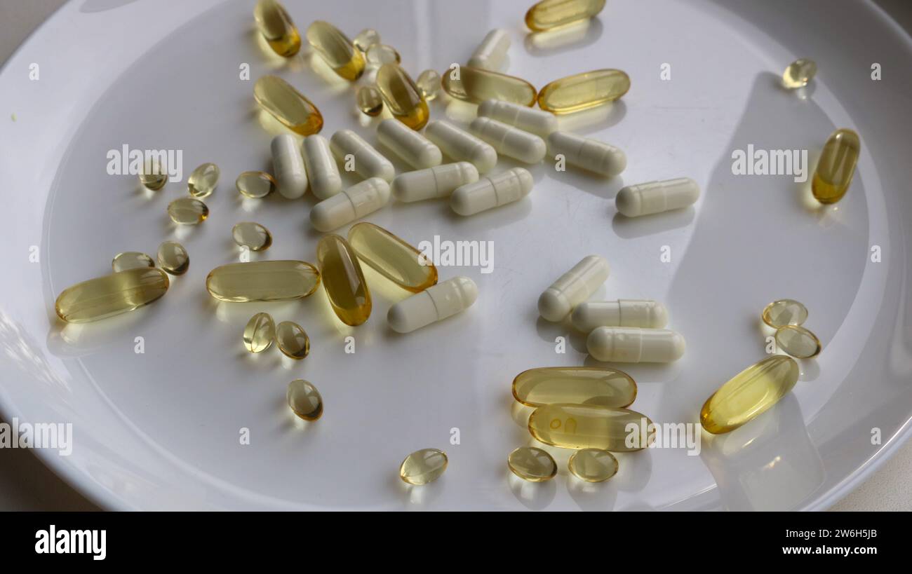 capsule di oro e bianco su un piatto grande come concetto per assumere vitamine con i pasti o, invece di cibo, integratori artificiali adagiati su un piatto Foto Stock