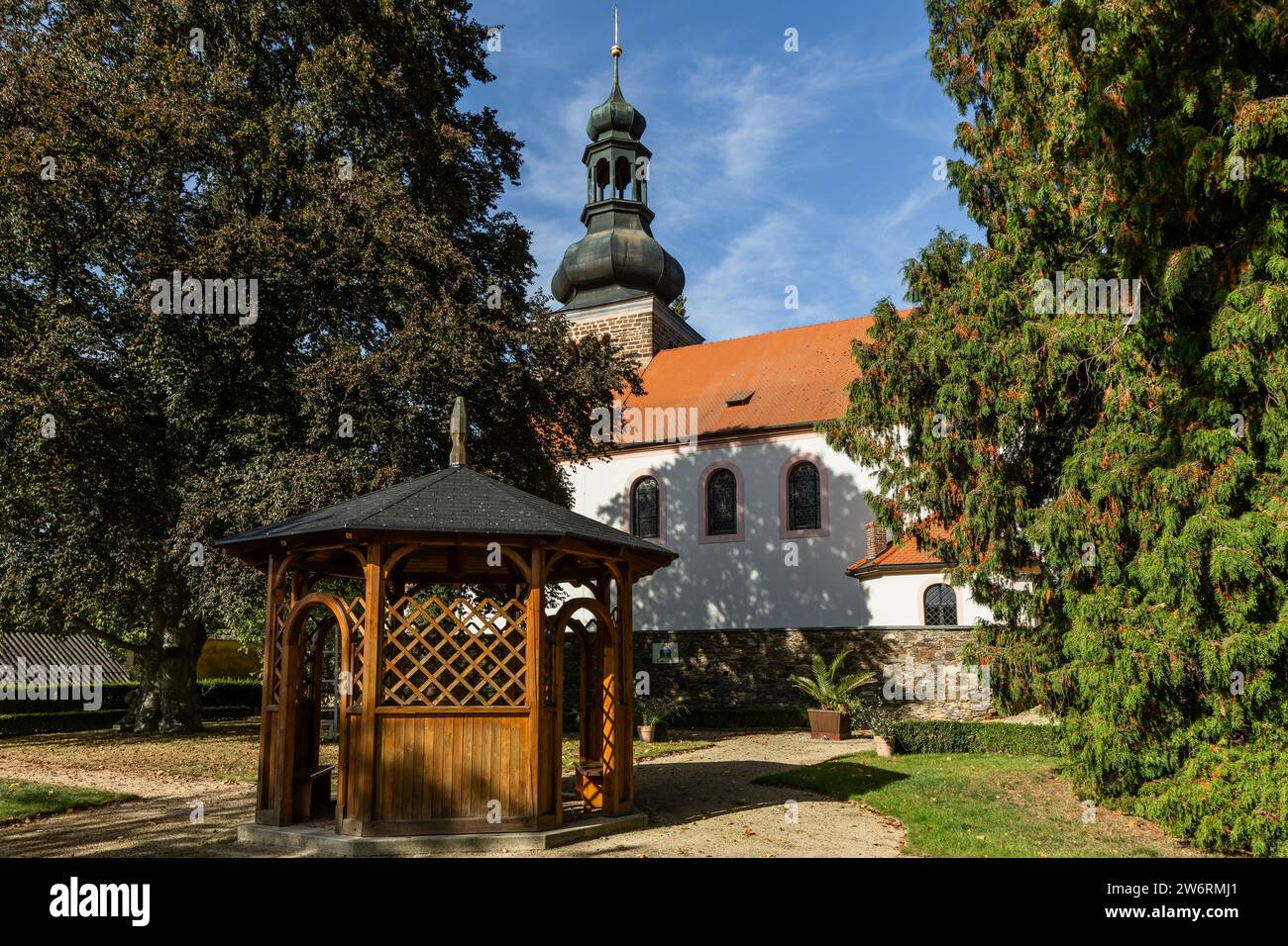 Svojsin, Repubblica Ceca - 13 ottobre 2023: Vista della chiesa di San Pietro e Pavel con la torre romanica in pietra, una casa estiva in legno, alberi verdi Foto Stock