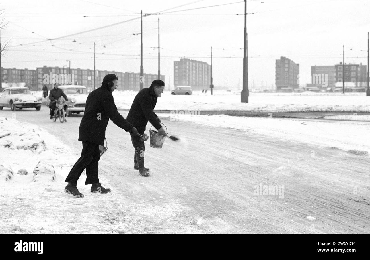 Le strade di Amsterdam si sono trasformate in piste di ghiaccio. Due uomini che spargono sale su strade ghiacciate, ca. 16 gennaio 1963 Foto Stock