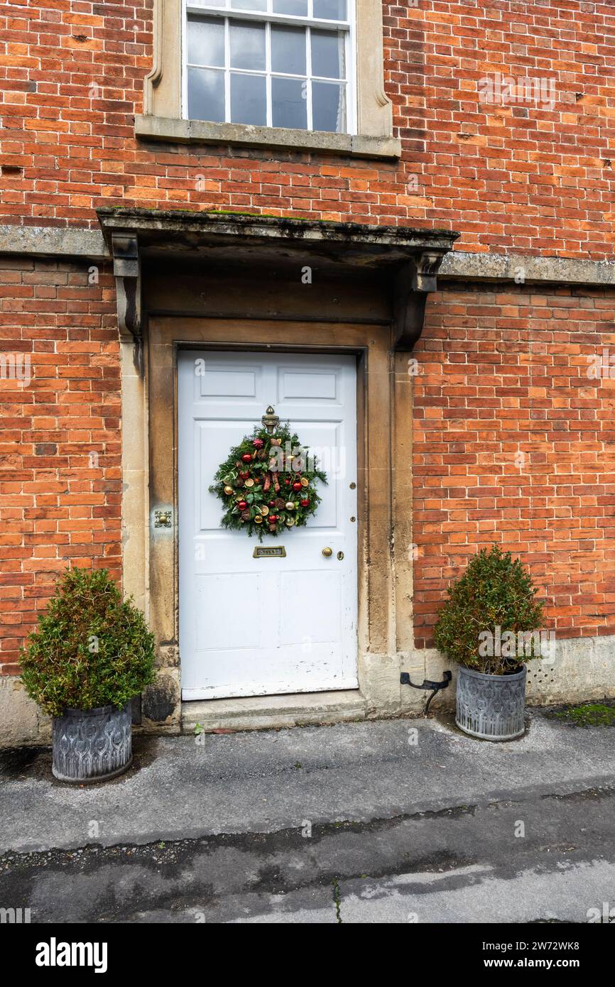 Primo piano di una porta d'ingresso bianca con corona di Natale su una casa in mattoni rossi nel villaggio National Trust di Lacock, Wiltshire, Inghilterra, Regno Unito Foto Stock