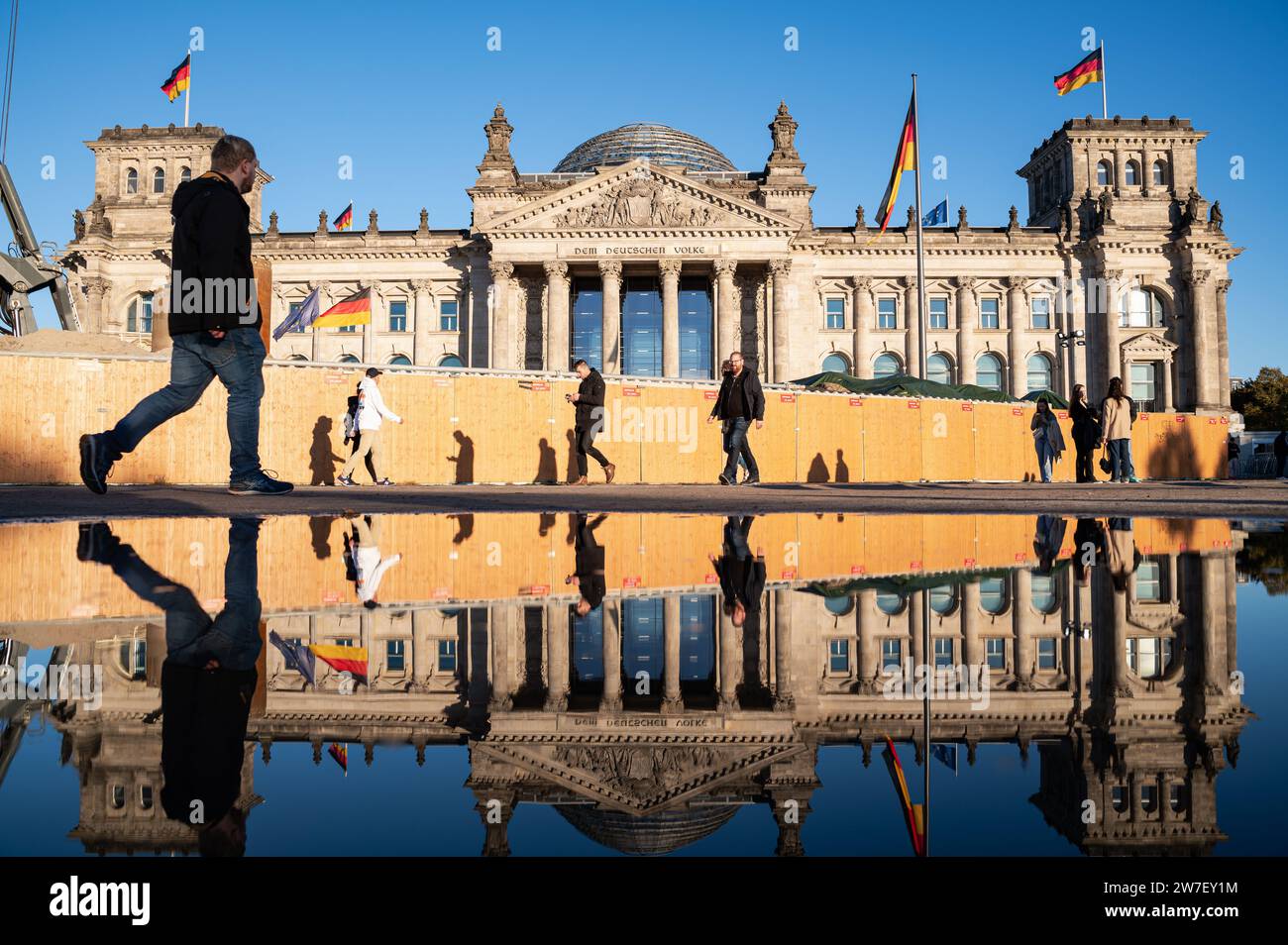 21.10.2023, Germania, Berlino, - la gente cammina davanti al Reichstag nel quartiere Mitte di Berlino in una soleggiata giornata autunnale, la sua faÁade occidentale si riflette in una grande Foto Stock