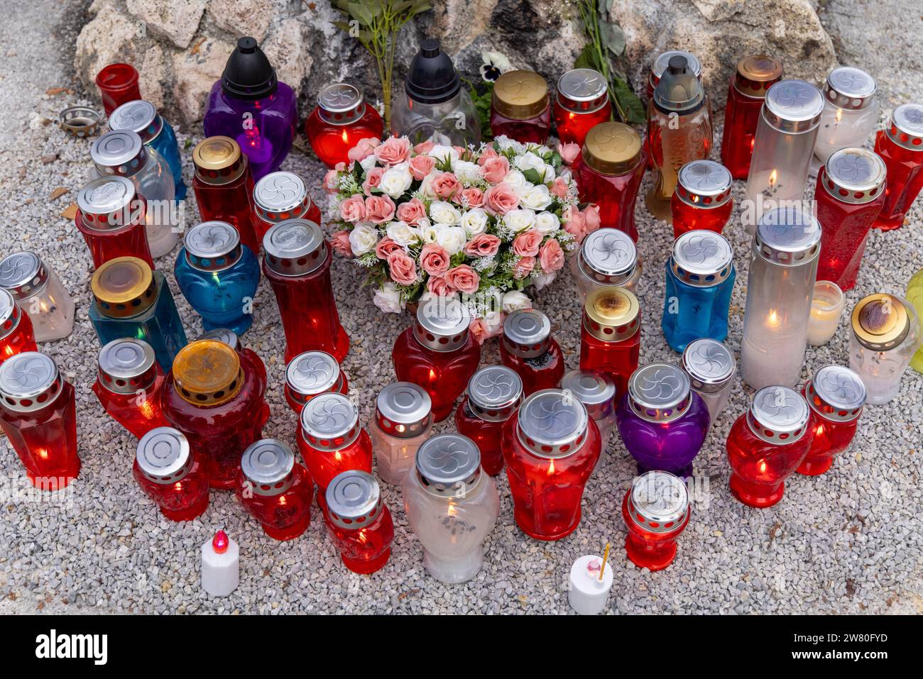 Molte candele funerarie (candele commemorative) in portatori di vari colori (blu, rosso, contenitori trasparenti) su un cimitero; con fiori; viste dall'alto Foto Stock
