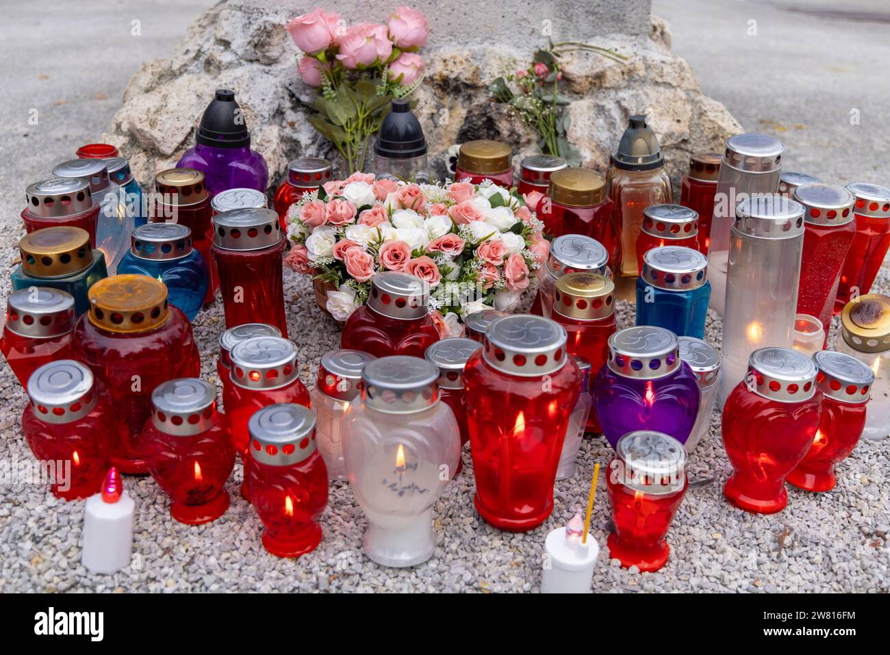 Varie candele funerarie (candele commemorative) in vasi di vari colori (blu, rosso, contenitori trasparenti) su un cimitero; con fiori Foto Stock