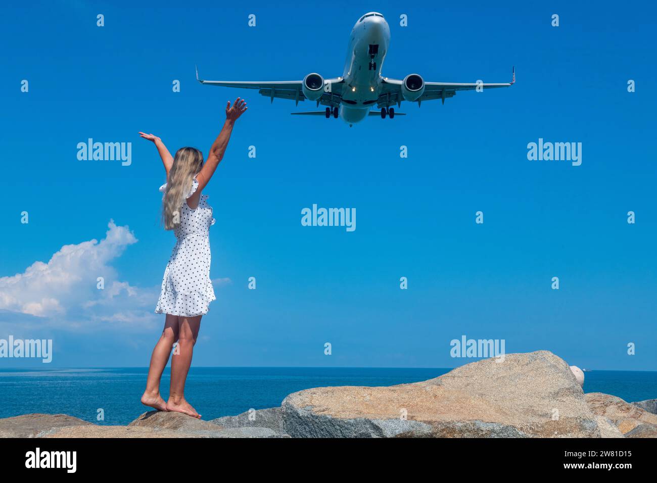 Oceanic Connection: Una ragazza con un abito bianco su pietre incontra un aereo volante Foto Stock