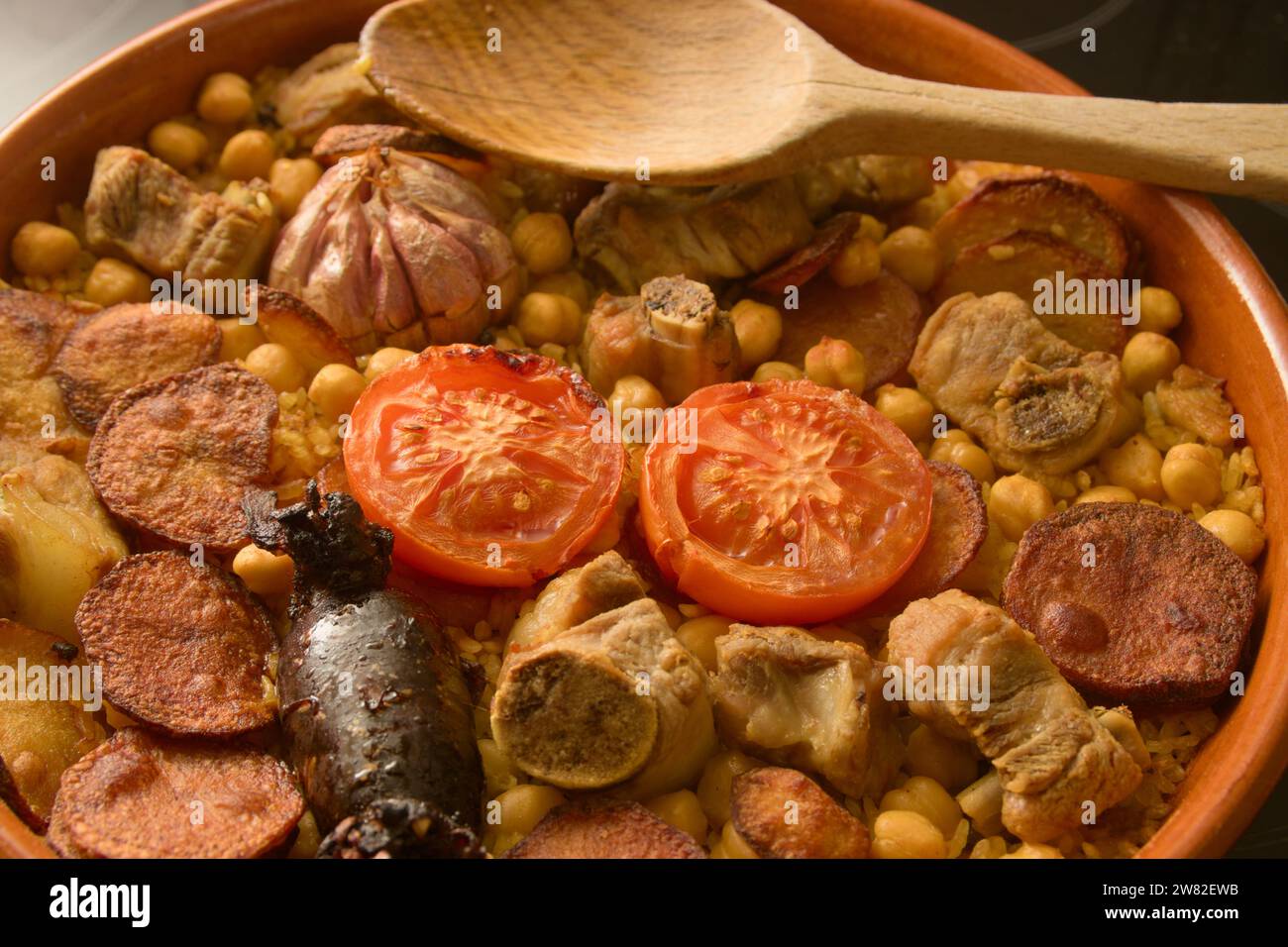 Primo piano di una casseruola di riso al forno, un tipico piatto valenciano con salsiccia di sangue, patate, ceci, costolette accanto a un cucchiaio di legno Foto Stock Primo piano di una casseruola di riso al forno, un tipico piatto valenciano con salsiccia di sangue, patate, ceci, costolette accanto a un cucchiaio di legno Foto Stock