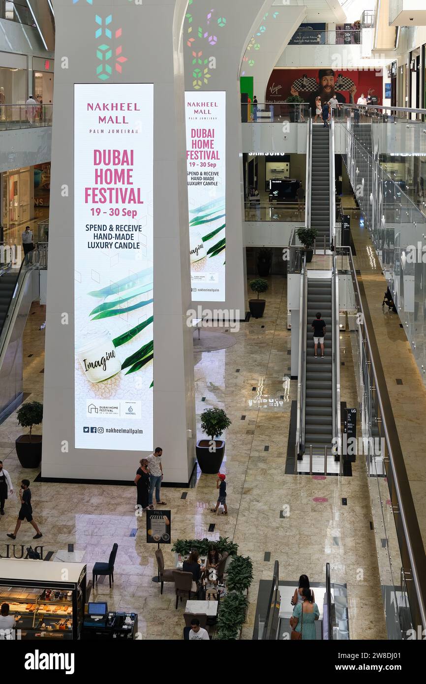 Acquirenti, scale mobili e grandi colonne pubblicitarie nel Nakheel Mall a Palm Jumeirah, Dubai, Emirati Arabi Uniti Foto Stock