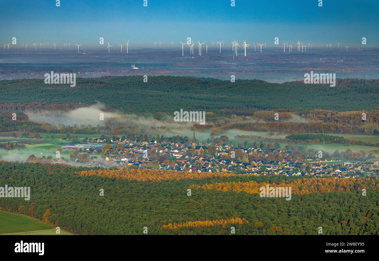Vista aerea, nebbia sul villaggio di Hullern con St Andreas Church, parco delle turbine eoliche sullo sfondo, circondato da alberi decidui autunnali, Hu Foto Stock