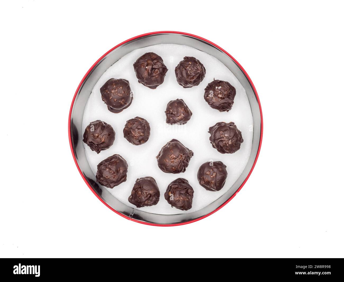 Contenitore rotondo di caramelle di pan di zenzero svedesi fatte in casa, ricoperte di cioccolato fondente e cosparse di scaglie di sale, su uno sfondo bianco. Foto Stock