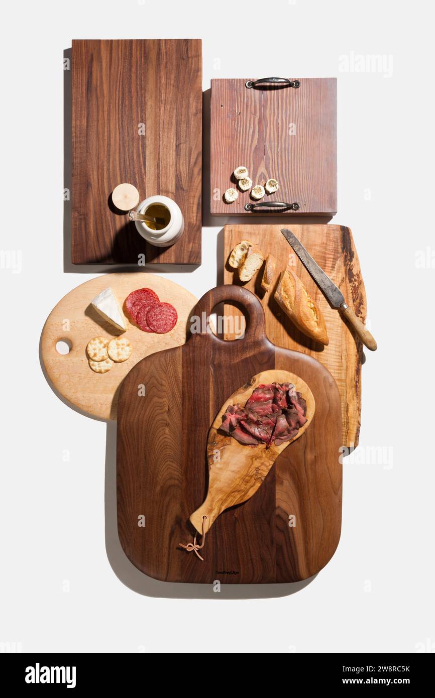 Vista ad angolo elevato di un assortimento di taglieri di legno con carni, formaggi, pane e cracker preparati su sfondo bianco Foto Stock