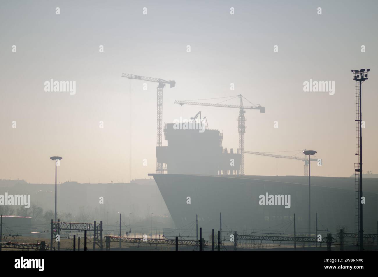 gru da cantiere nella nebbia, una città che sta crescendo con nuovi edifici, la nebbia e le sagome dei cantieri in lontananza. Foto Stock