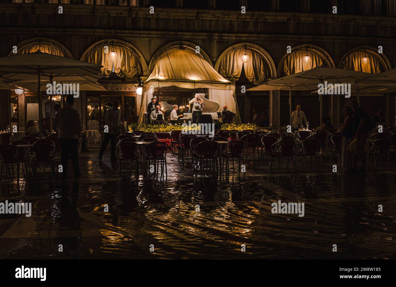 Piazza Marco a Venezia, in Italia, la sera piovosa con un gruppo di musicisti che suonano sotto la tenda del ristorante; luci che si riflettono nelle pozzanghere Foto Stock