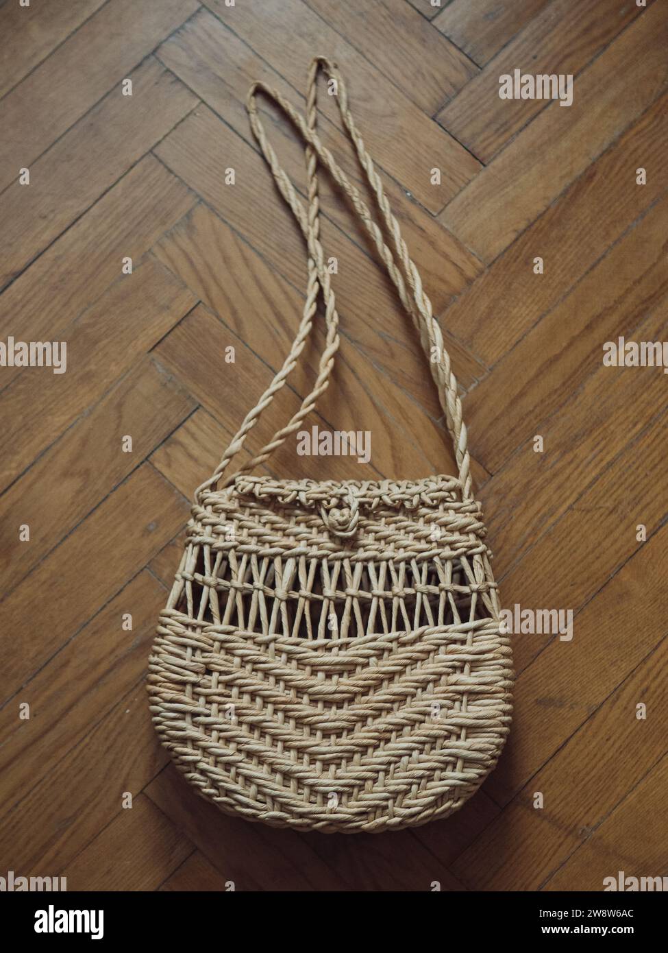Immagine verticale dall'alto di una borsa da spiaggia con spalla di paglia sul pavimento in parquet. Foto Stock