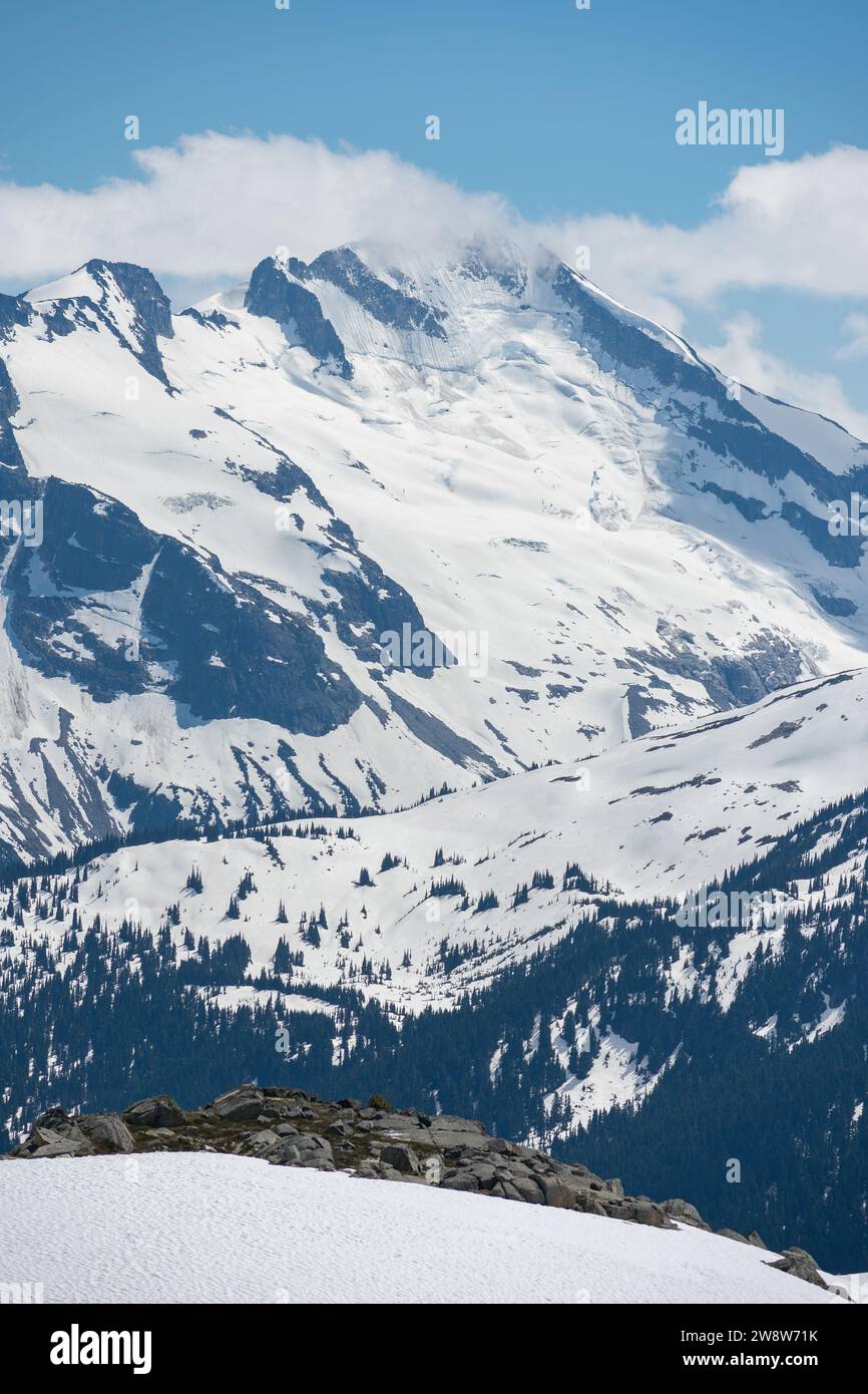 Una vista mozzafiato si apre dal monte Whistler, mostrando le vaste cime innevate delle Montagne Rocciose canadesi contro un cielo azzurro. Foto Stock
