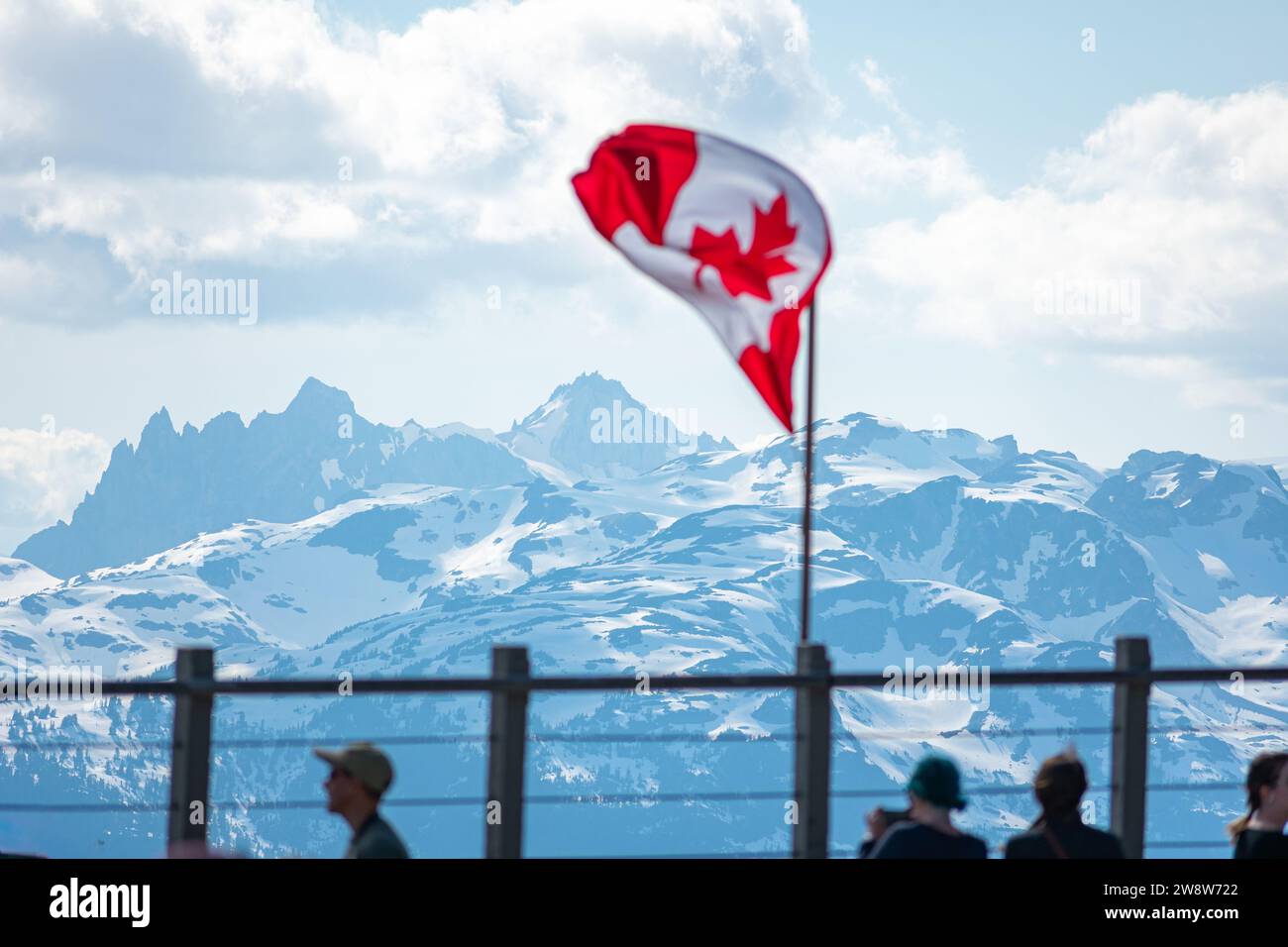 La bandiera canadese sventola con orgoglio sullo sfondo delle cime innevate del monte Whistler, a simboleggiare lo spirito di avventura nella Columbia Britannica. Foto Stock