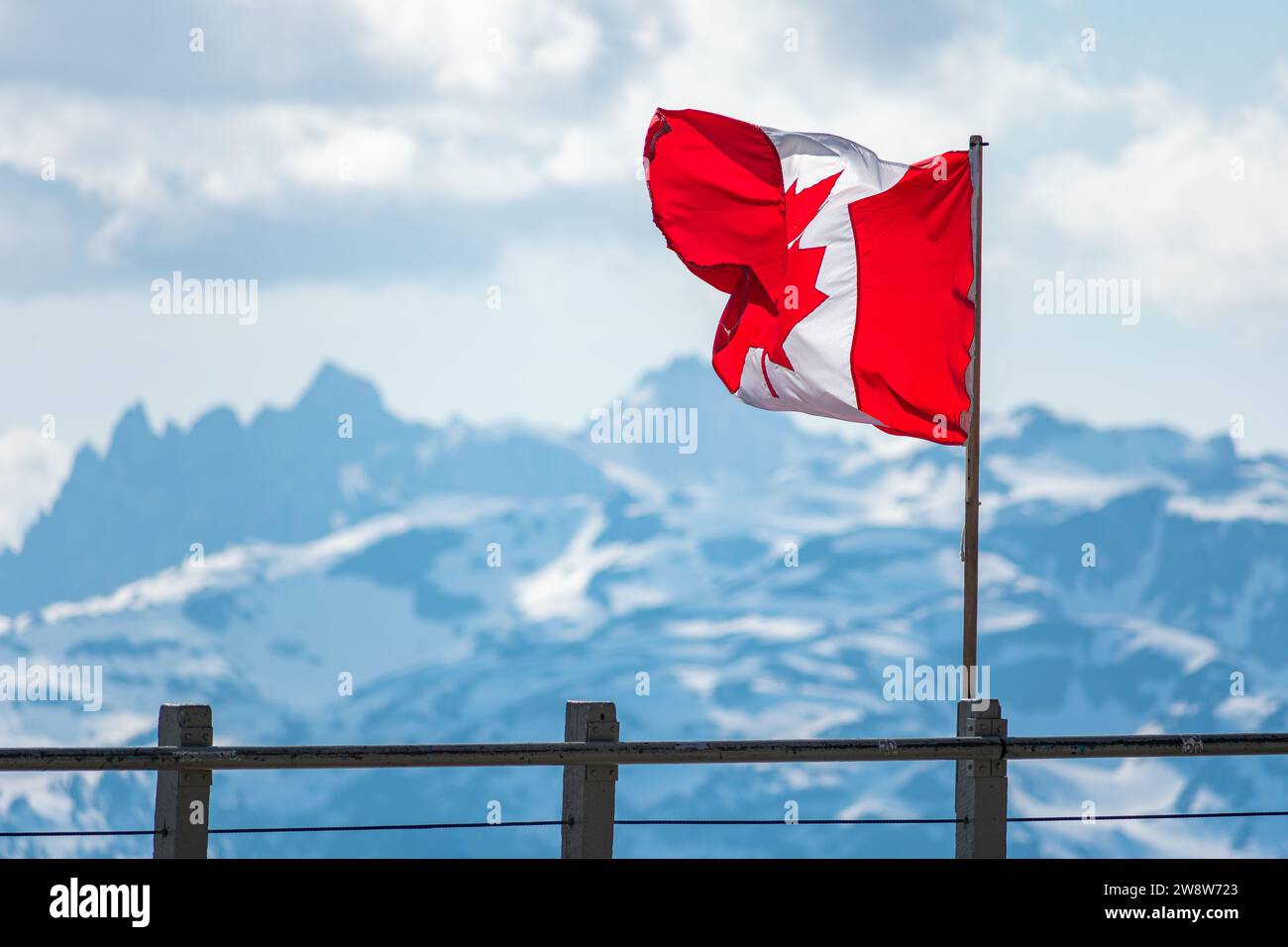 La bandiera canadese sventola con orgoglio sullo sfondo delle cime innevate del monte Whistler, a simboleggiare lo spirito di avventura nella Columbia Britannica. Foto Stock