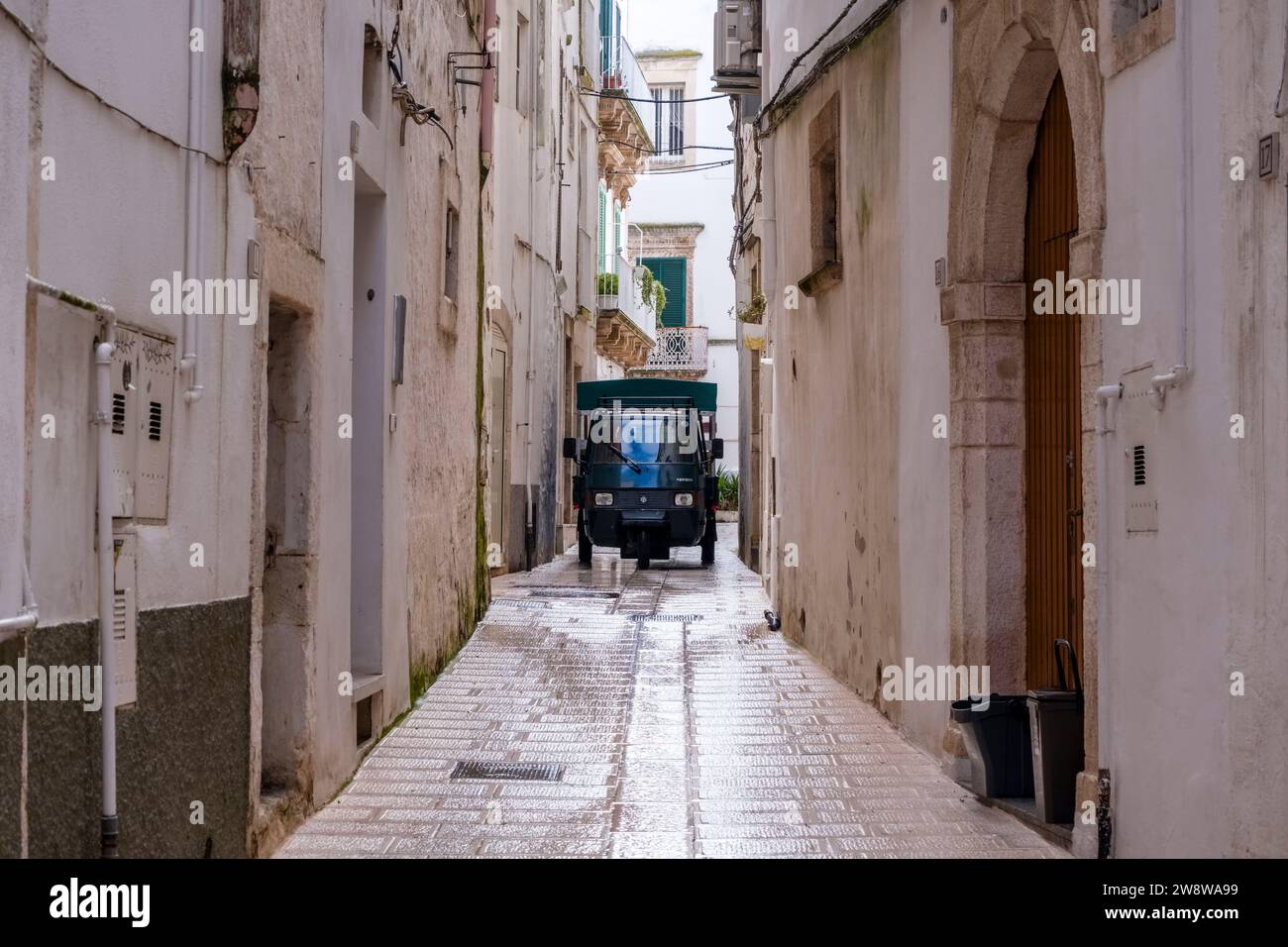 Una Piaggio Ape, un veicolo commerciale leggero a tre ruote, guida lungo una piccola strada tra case dipinte di bianco. Foto Stock