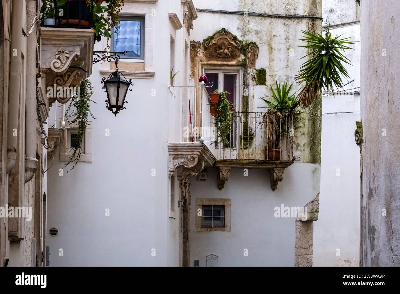 Scena di strada con un piccolo cortile tra case, balconi e piante verdi in vaso. Foto Stock