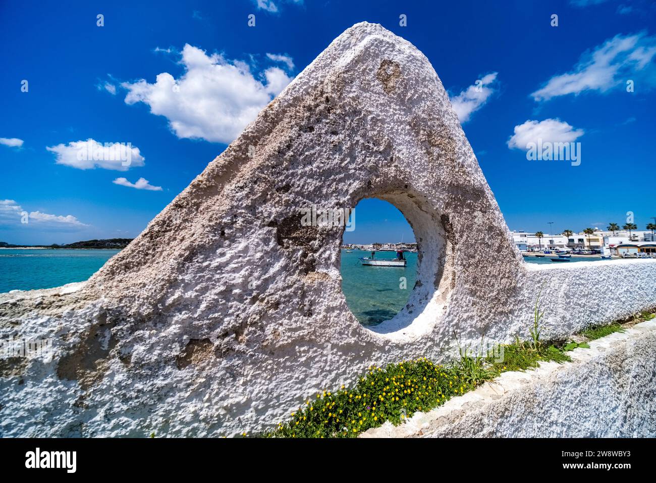 Case e porticciolo sulla riva della cittadina, un peschereccio all'ancora nella baia poco profonda, visto da una finestra su un muro bianco. Foto Stock