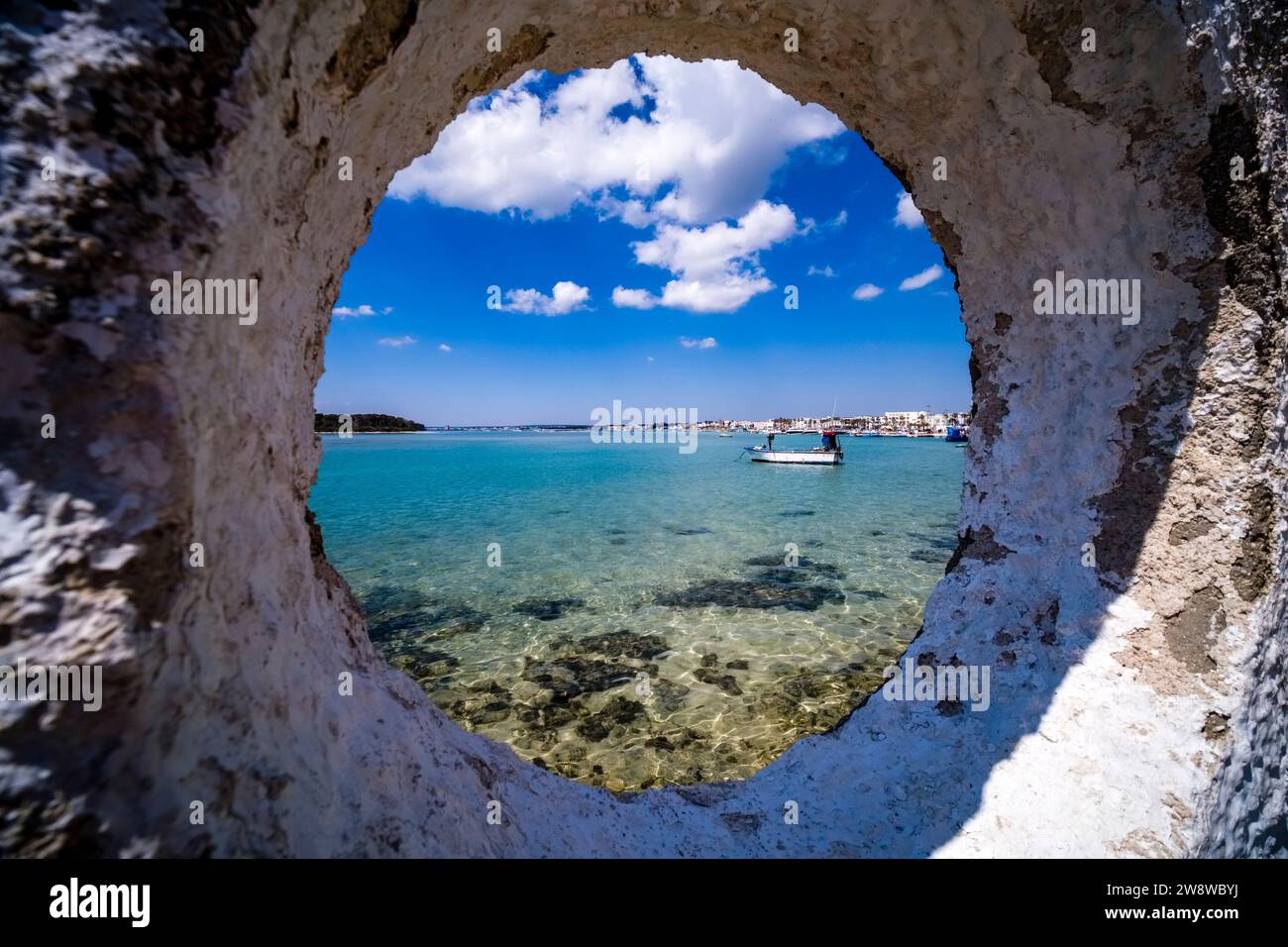 Case e porticciolo sulla riva della cittadina, un peschereccio all'ancora nella baia poco profonda, visto da una finestra su un muro bianco. Foto Stock