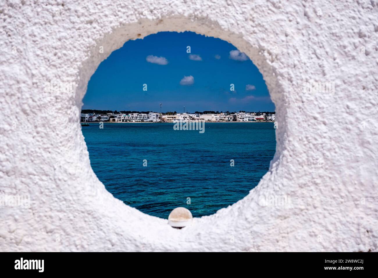 Case sulla riva della piccola città, un peschereccio all'ancora nella baia poco profonda, visto da una finestra su un muro bianco. Foto Stock