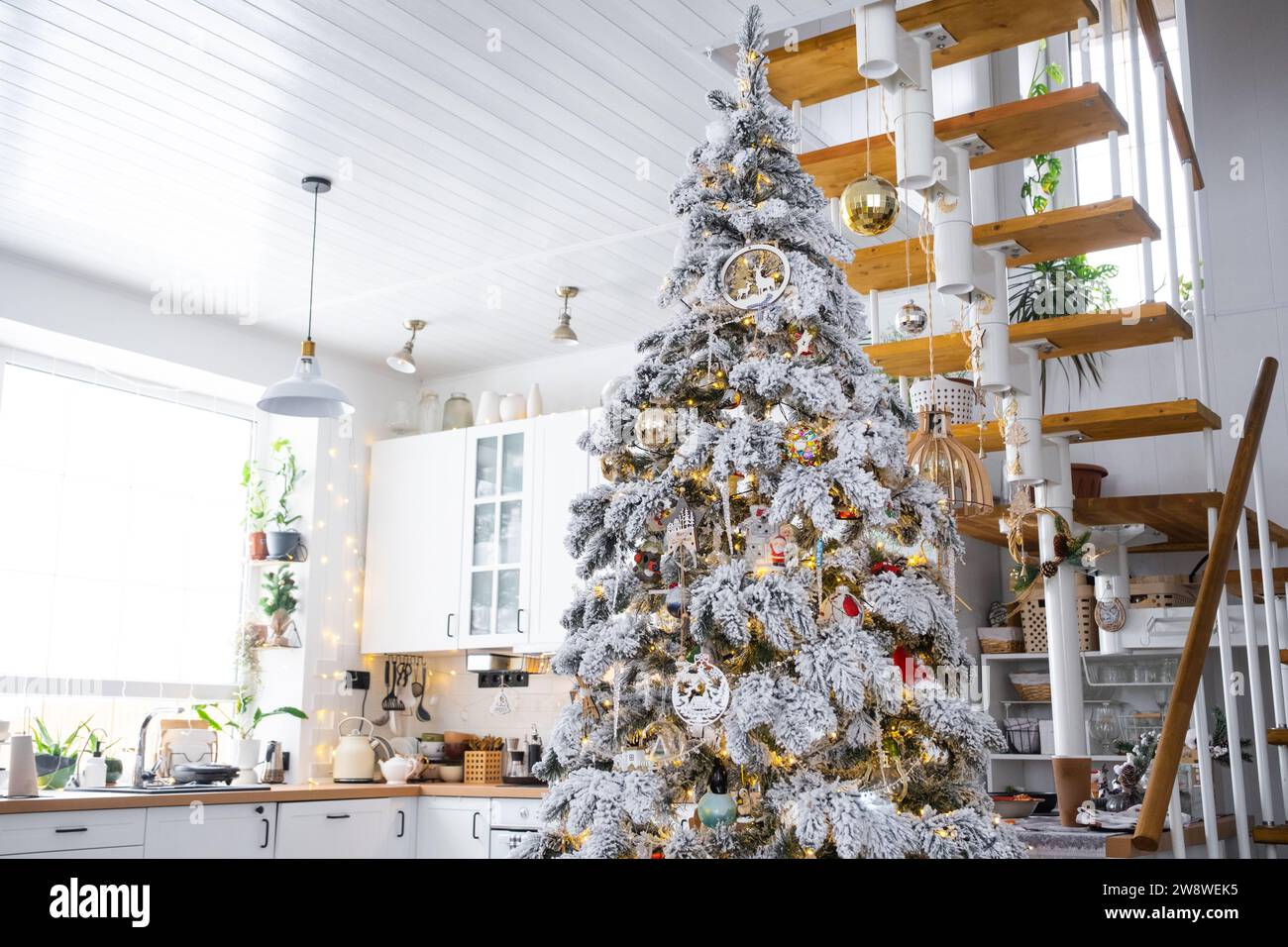 Decorazioni natalizie natalizie in cucina bianca, interni moderni del villaggio con un albero di Natale innevato e luci delle fate. Capodanno, atmosfera natalizia, casa accogliente, M Foto Stock